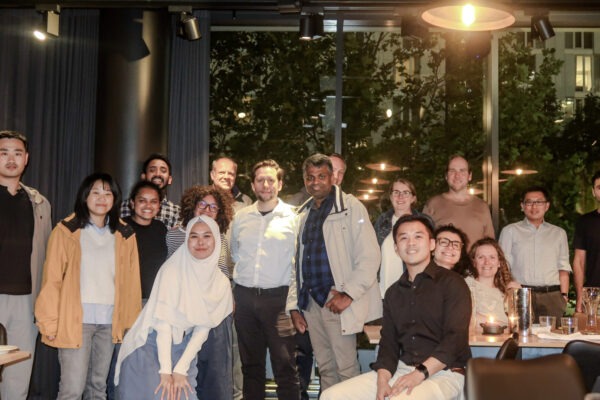 Photo of POSEIDON participants in a group smiling at the camera. The surroundings are dimly lit in a restaurant setting, with a couple of warm lights in the shot.