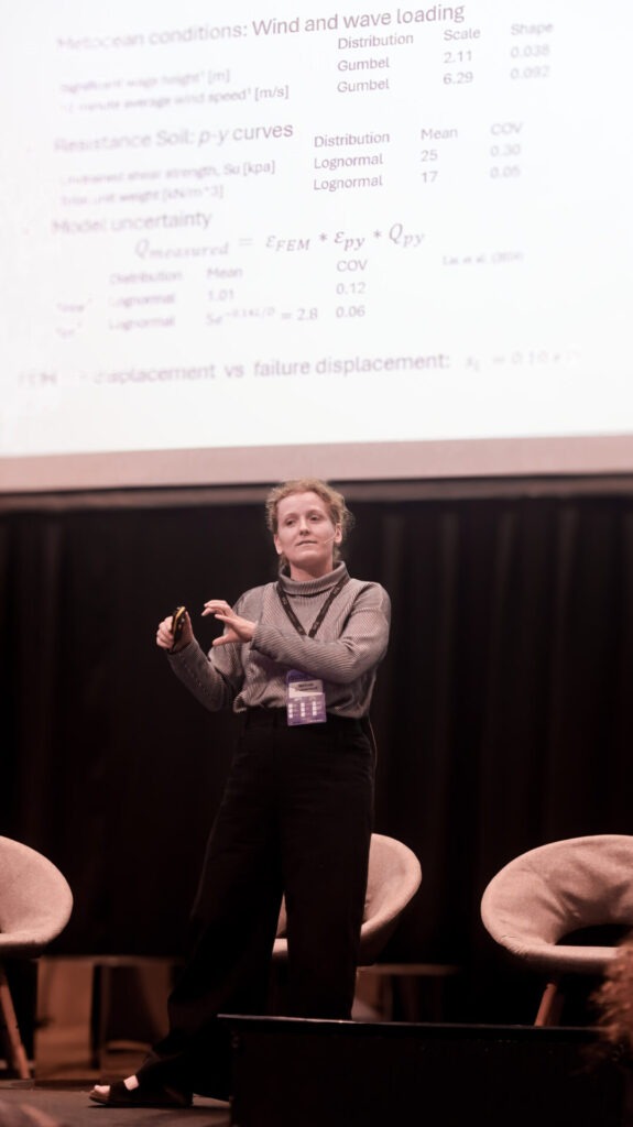 Photo of Mathilde wearing a mic on stage with a slide projected behind her.